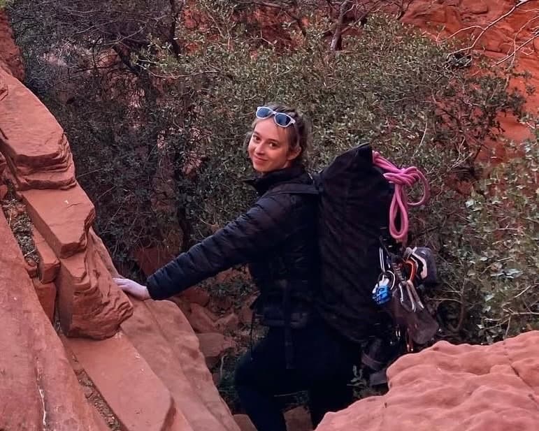 Sophie, a Dogwood Mountain School instructor, smiling in red rock country with a climbing pack and pink rope.